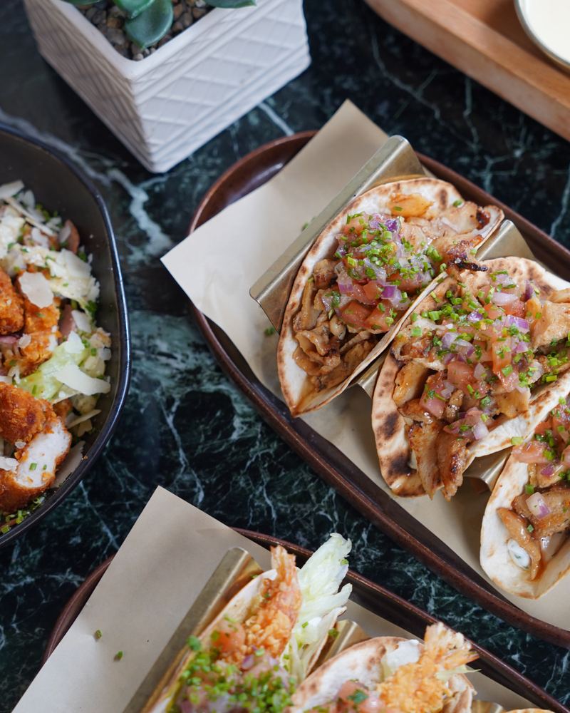 Pork soft tacos topped with pico de gallo and chives served beside crispy salad bowls on green marble