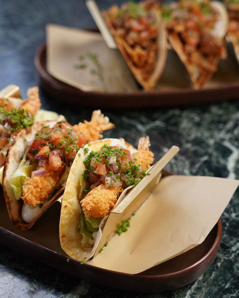 Close-up of crispy shrimp tacos with lettuce, pico de gallo and fresh chives in brass taco holders