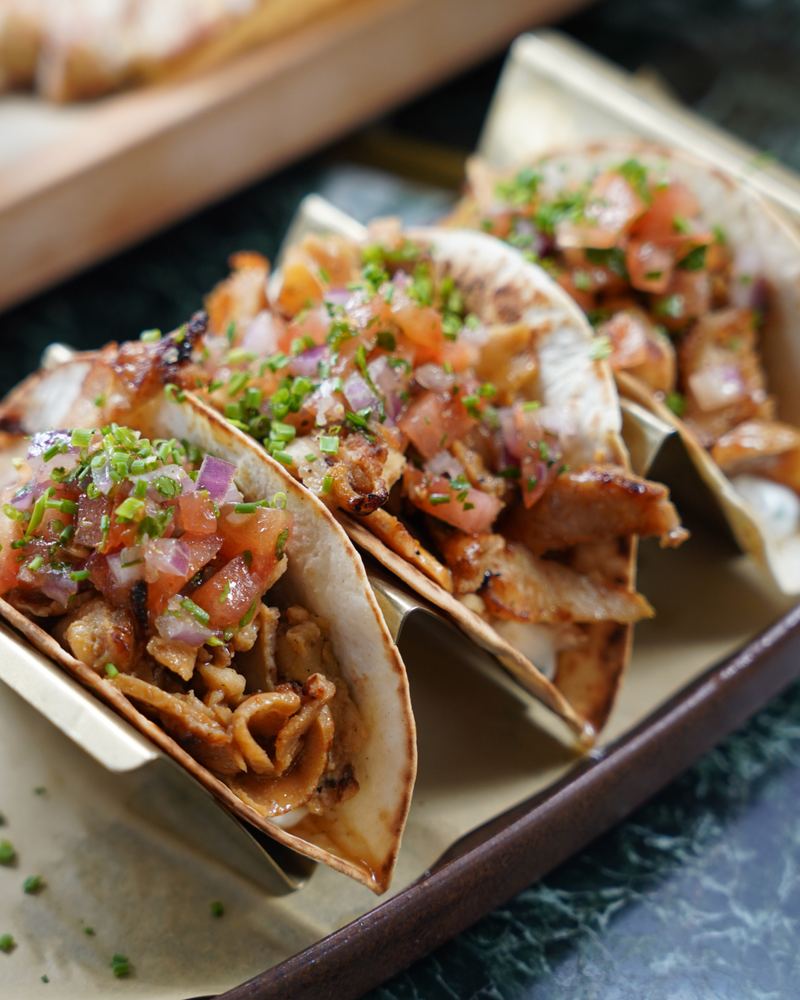 Close-up of grilled pork tacos filled with caramelised meat, fresh tomato salsa and chopped chives