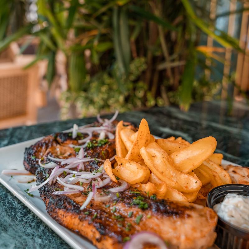 Charred grilled fish fillet topped with red onion and parsley, served with seasoned potato wedges and tartare sauce
