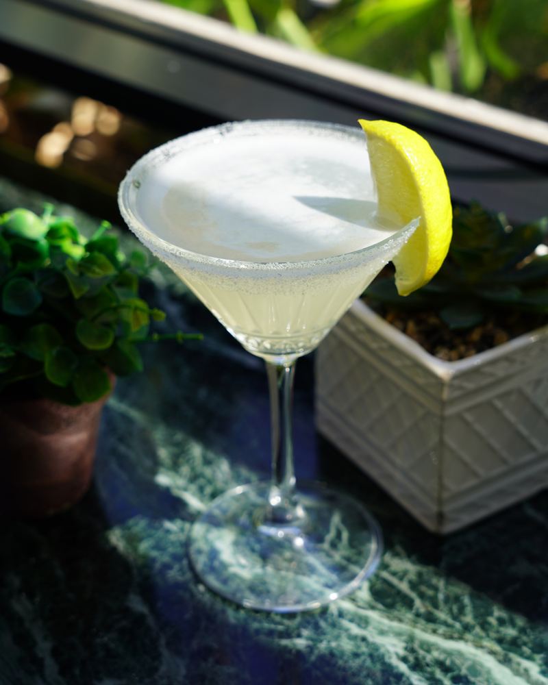 Chilled citrus cocktail in a stemmed glass with a sugared rim and lemon wedge on a green marble table