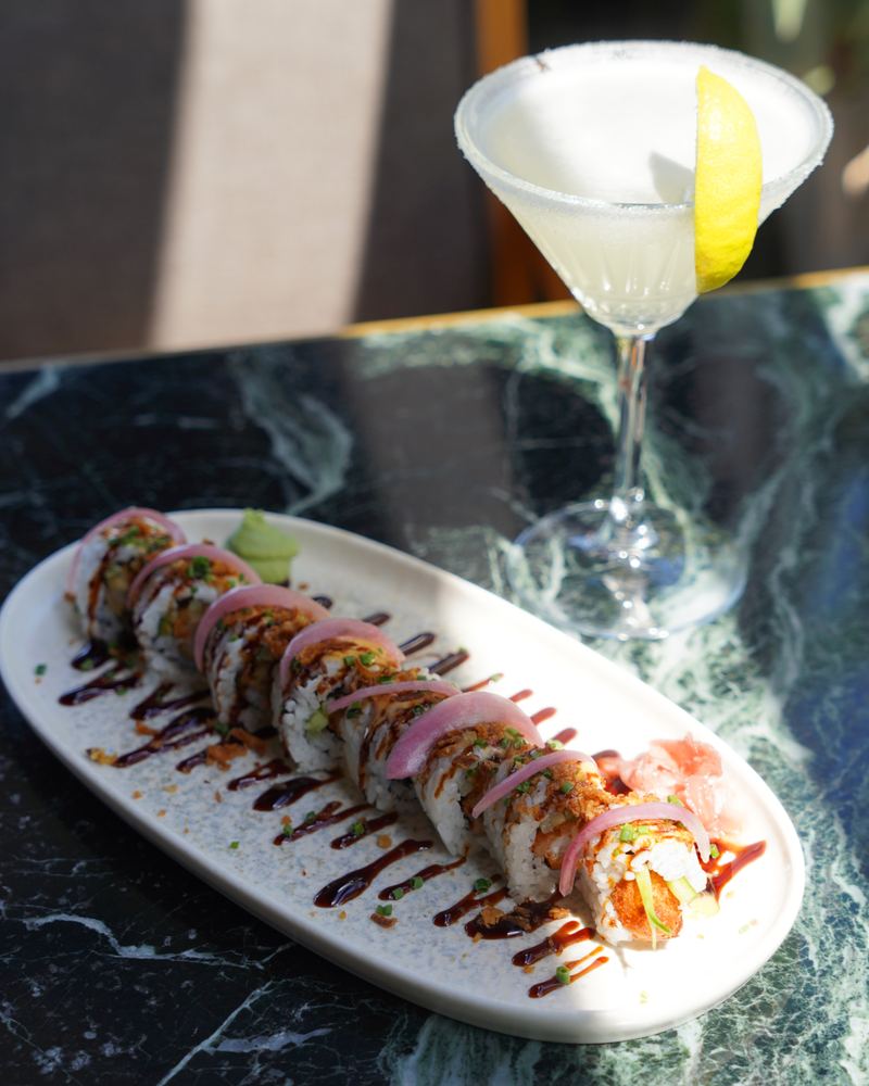 Citrus martini with a lemon wedge served alongside a plated sushi roll at Al Hayat Resto Bar