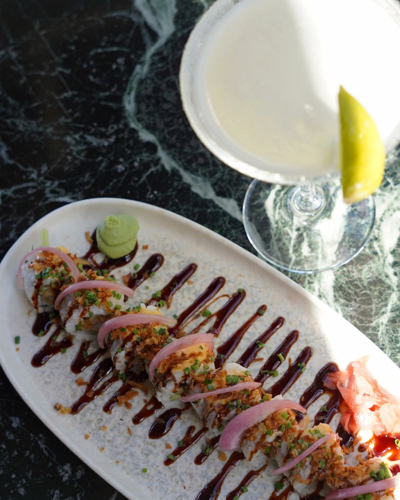 Overhead view of a citrus cocktail and sushi roll pairing on Al Hayat's green marble table