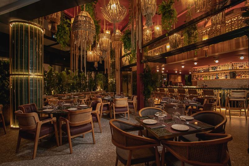 Al Hayat's main dining room with cane armchairs, green marble tables and cascading macramé chandeliers above a warm red ceiling