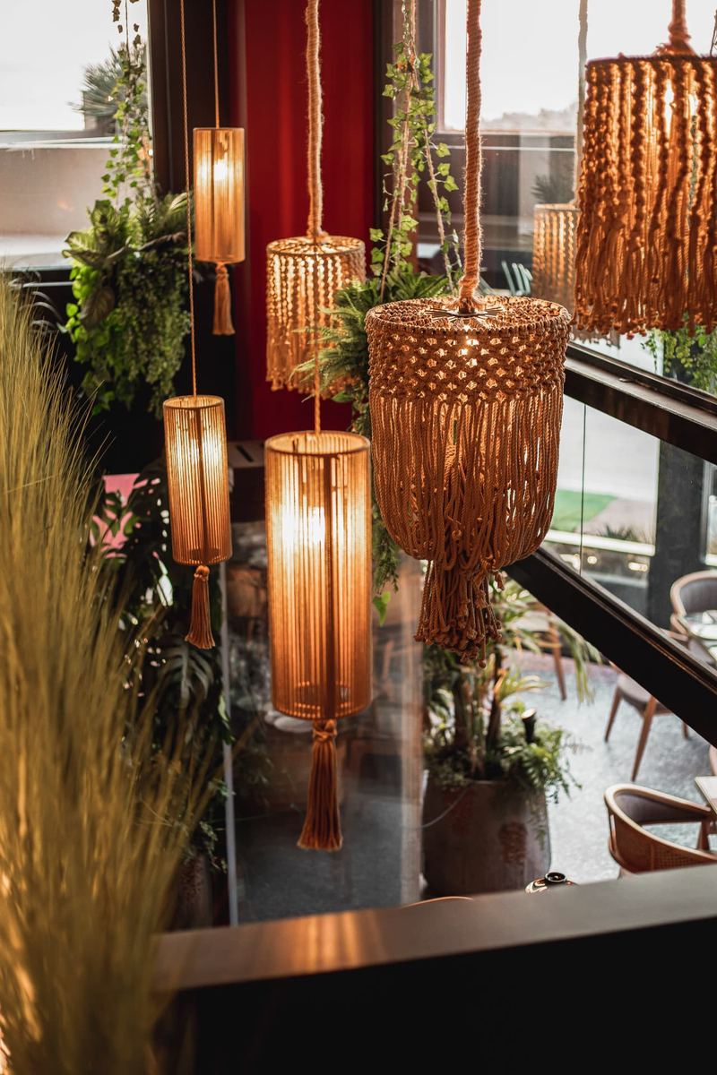 Cluster of handwoven macramé pendant lamps glowing gold against hanging greenery by the window at Al Hayat