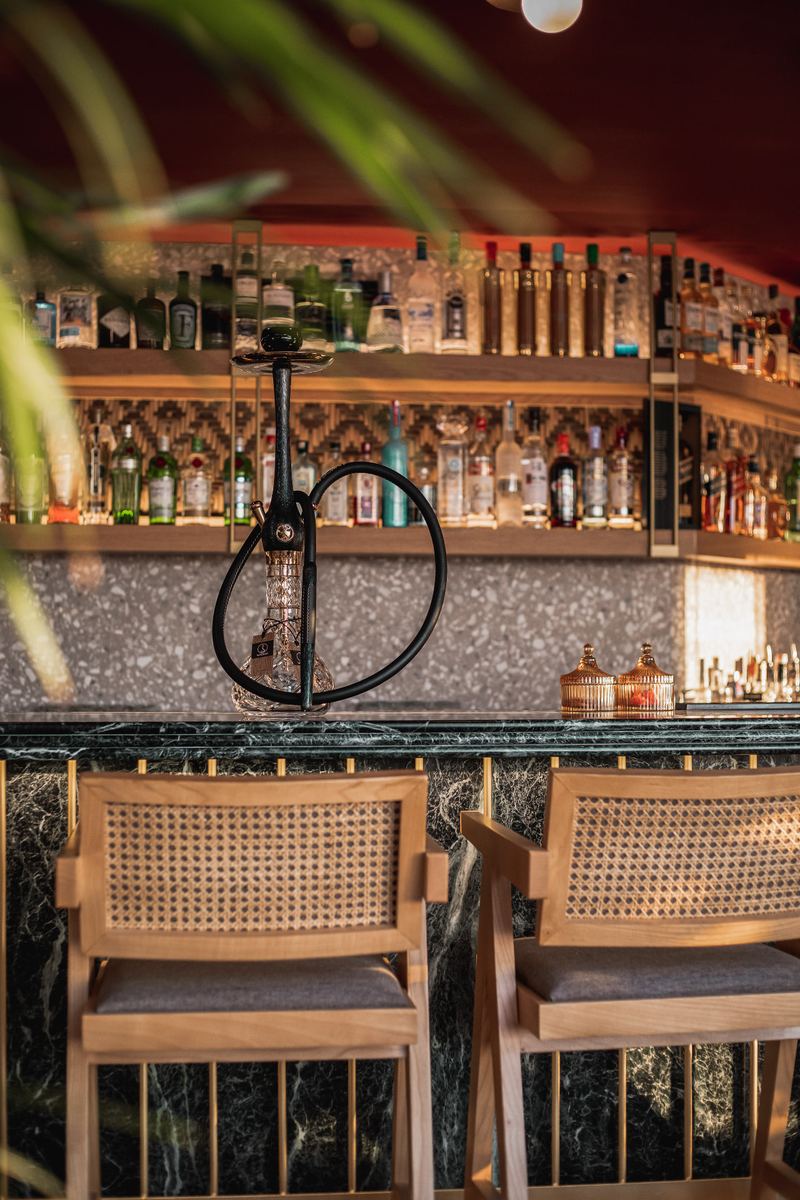 Crystal shisha resting on the green marble bar in front of backlit shelves of premium spirits and cane bar stools