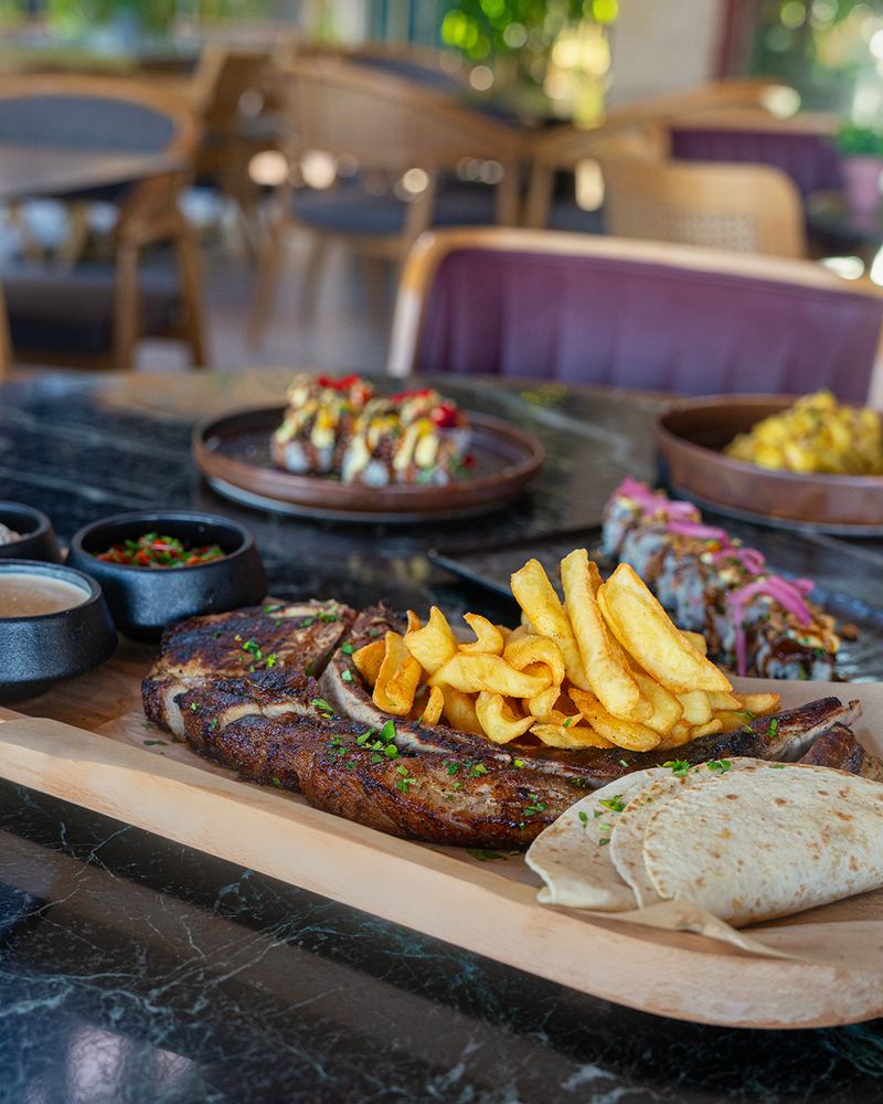 Grilled tomahawk steak sliced on a wooden board with fries and dipping sauces