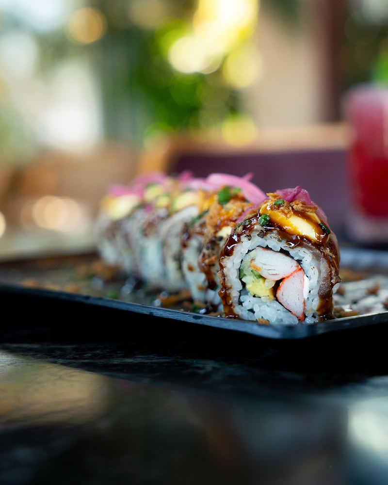 Signature sushi roll topped with salmon, avocado and sesame served on slate