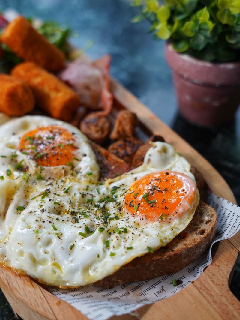 Full breakfast board with sunny-side-up eggs on sourdough, bacon, sausage and golden potato croquettes