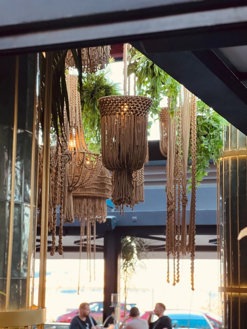 Handwoven macramé pendant lamps hanging above the lounge, framed by hanging greenery and gold-tone accents