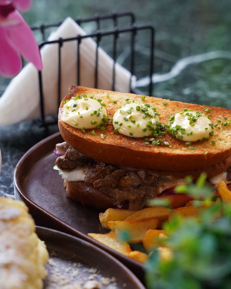 Grilled steak sandwich on toasted brioche topped with aioli dots and chives, served with golden hand-cut fries