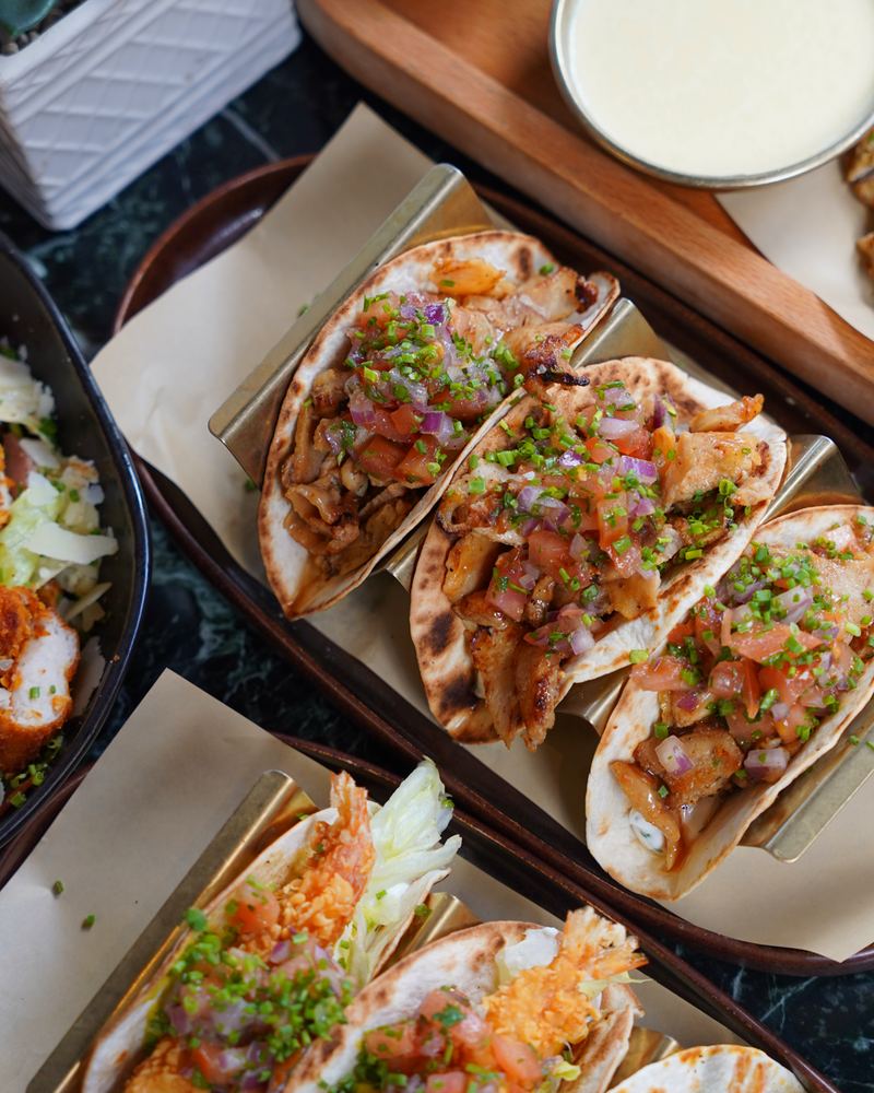 Grilled pork soft tacos topped with fresh pico de gallo and chives, served on brass taco holders
